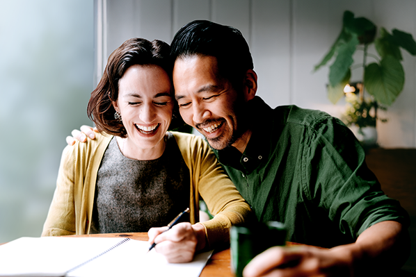 man and a woman laughing sitting at a table with an open notebook